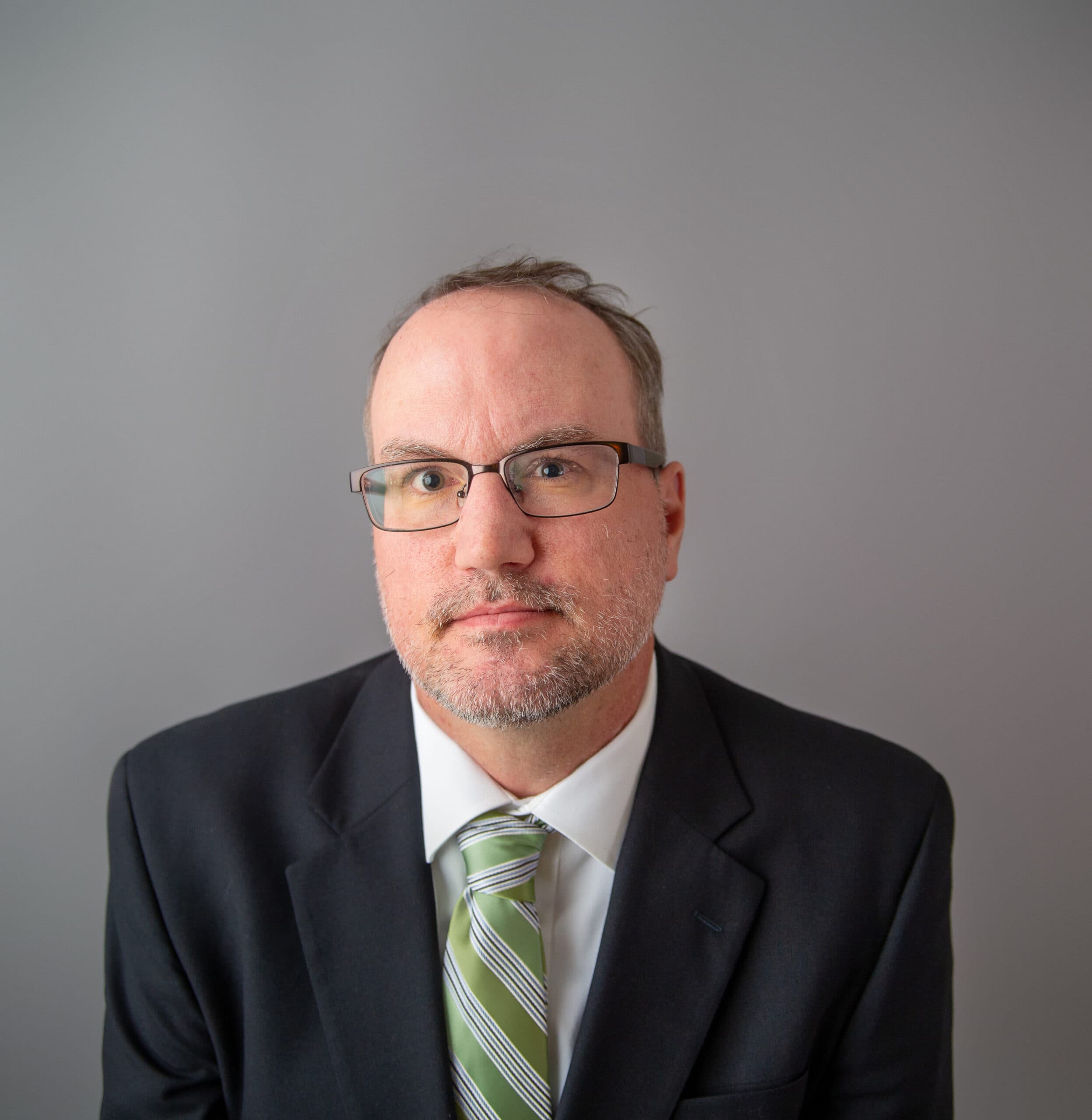 White man with glasses wearing a black suit and green tie