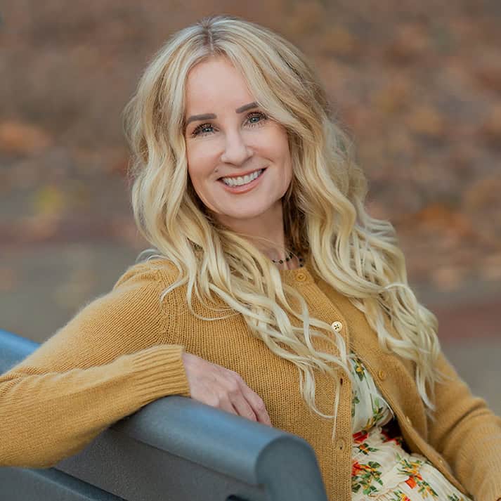 Blonde woman wearing a beige cardigan smiling.