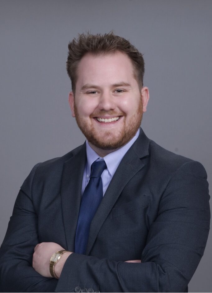 White man wearing a black and blue suit with a blue tie