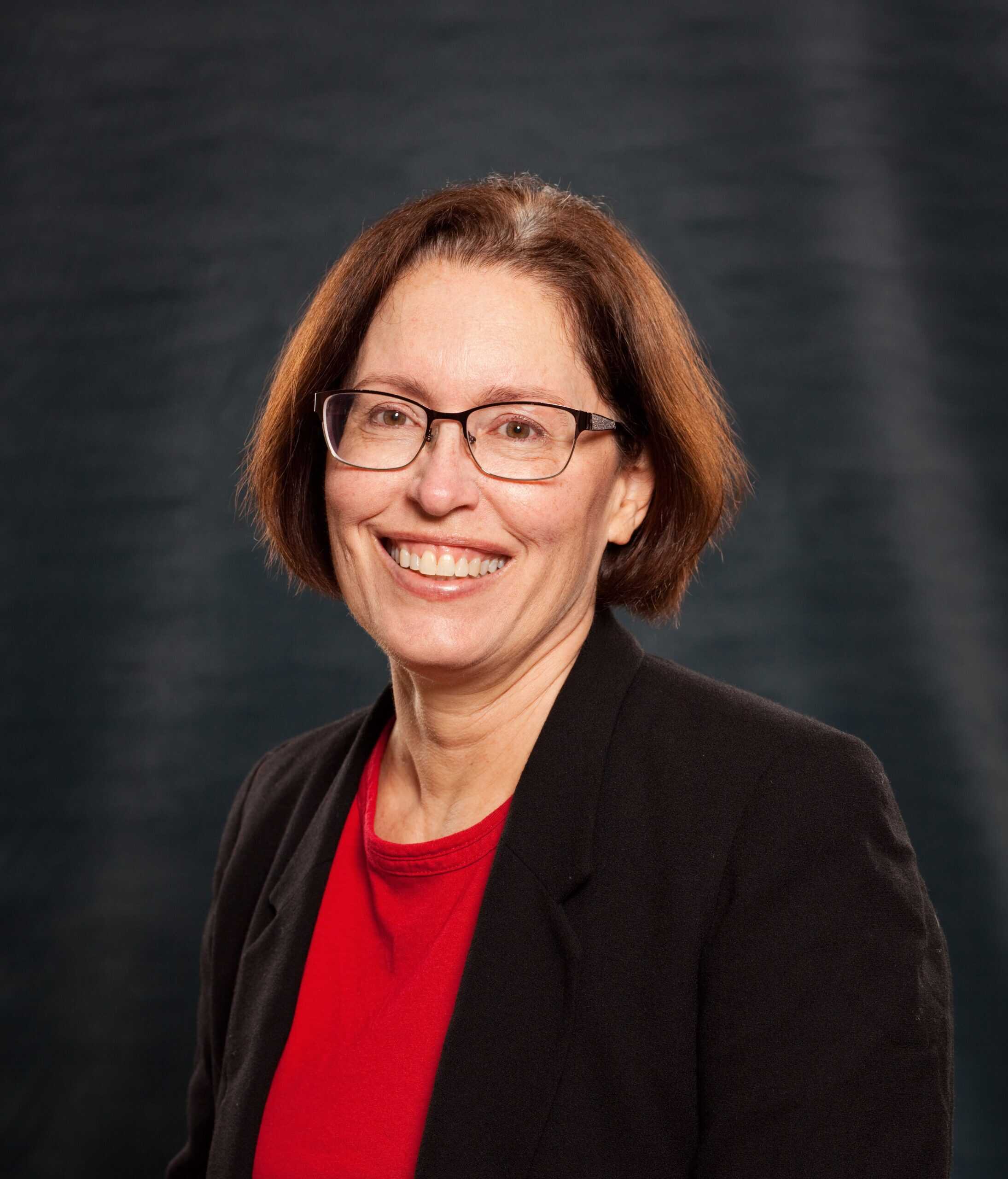 White woman with reddish-brown hair and wearing glasses smiling