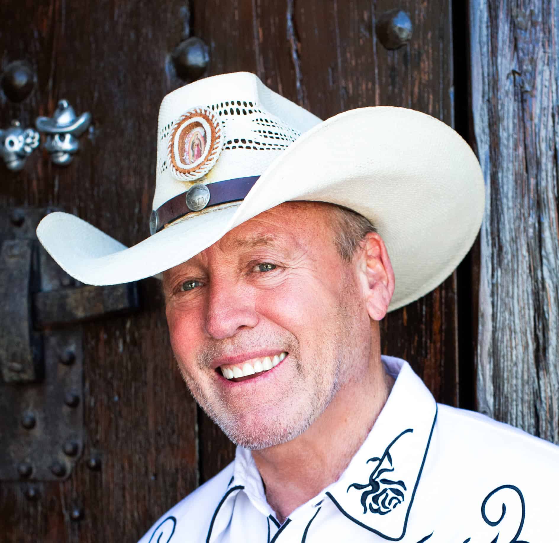 Gil Gillenwater headshot in a white western shirt with black accents and a white cowboy hat
