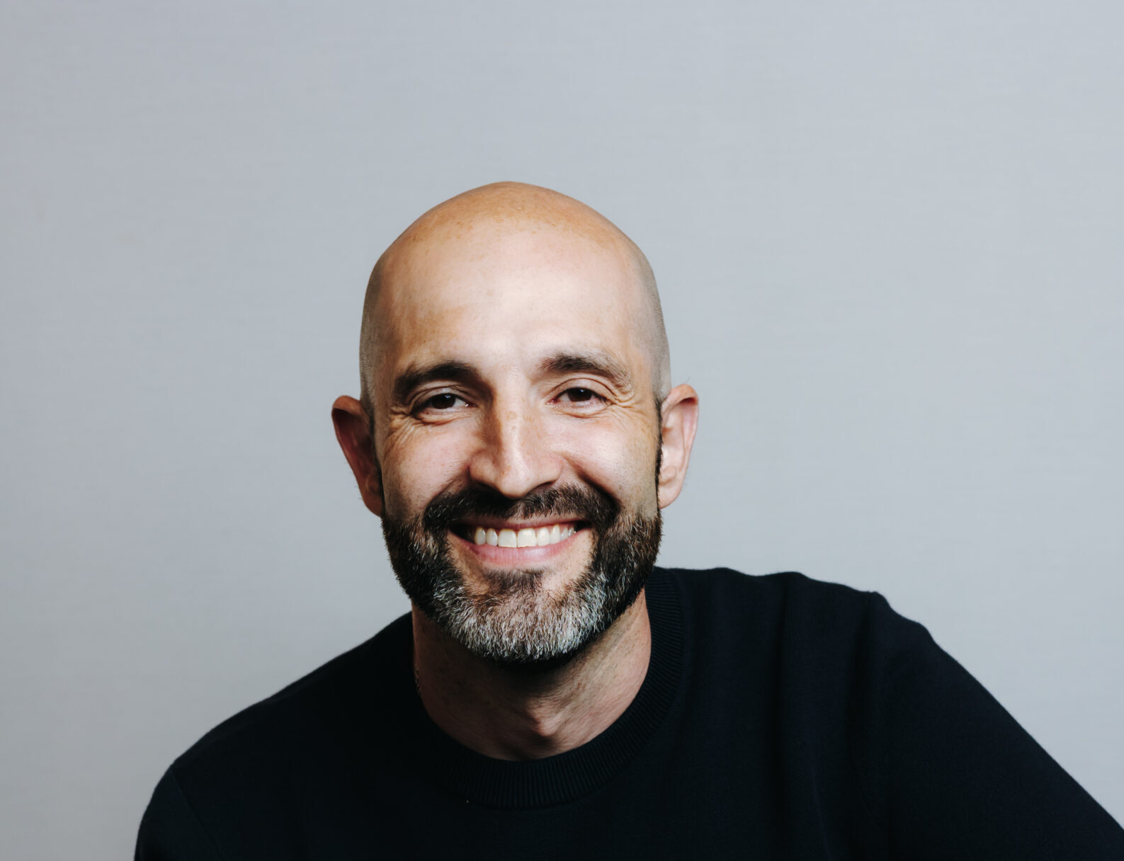 White man with a black and grey beard, wearing a black shirt, smiling