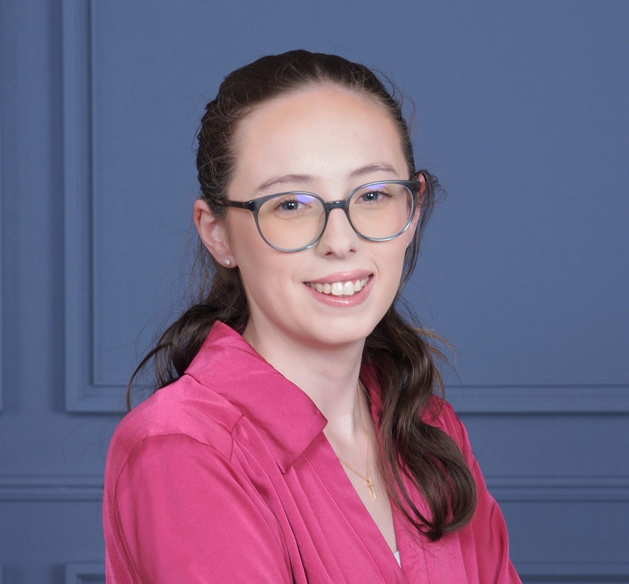 Woman with dark brown hair, wearing glasses and a pink blouse, smiling.