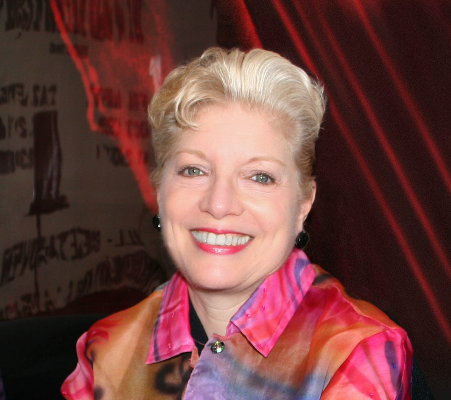 Woman with short, blonde hair wearing a colorful patterned dress and smiling